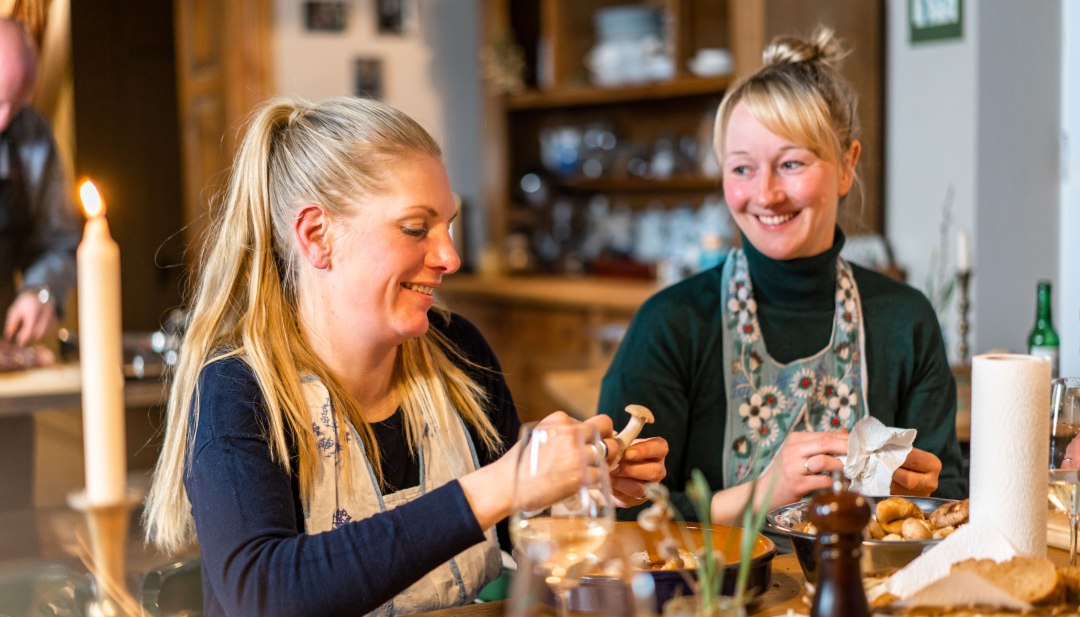 Zwei Frauen bereiten in der Küche im Gutshaus Ehmkendorf gemeinsam ein Essen zu, Kerzenlicht und Holzregale im Hintergrund. // Gemeinsam am langen Holztisch: frische Zutaten wandern in den Topf, Gespräch und Kerzenlicht füllen das Gutshaus Ehmkendorf. // © MV-T/Gross Zwei Frauen bereiten in der Küche im Gutshaus Ehmkendorf gemeinsam ein Essen zu, Kerzenlicht und Holzregale im Hintergrund.