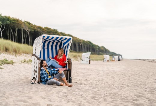 Ein Pärchen sitzt im Strandkorb am Strand von Graal-Müritz, © MV-T/Gross Pärchen sitzt in einem Strandkorb am Strand von Graal-Müritz an der Ostseeküste. Im Hintergrund ist der Küstenwald zu sehen.
