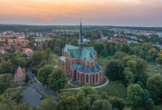 Luchtfoto van de kathedraal in Bad Doberan bij zonsondergang, omringd door bomen, weiden en de omliggende stad.
