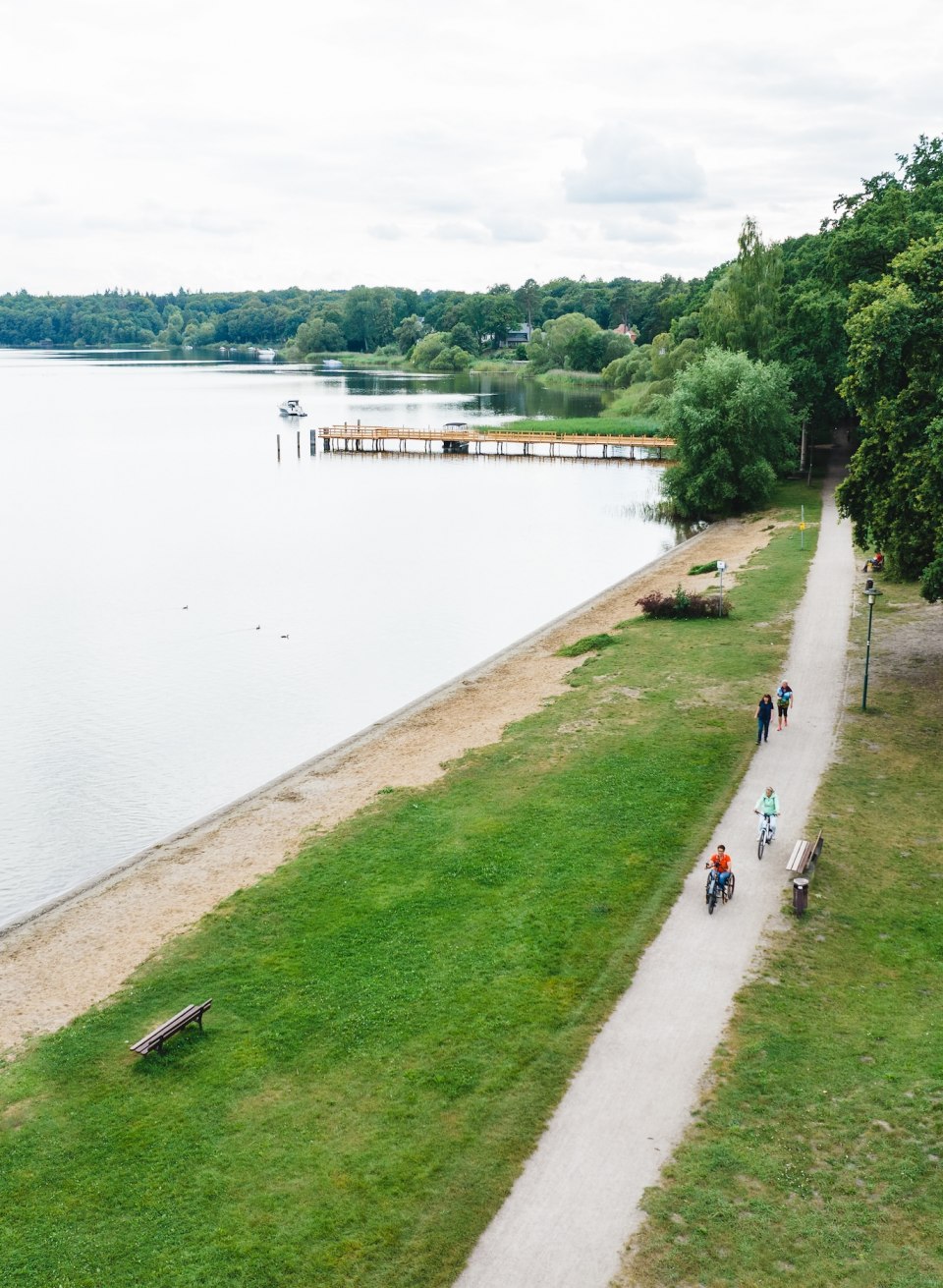 Eine Handbikerin und Fahrradfahrerin auf einem Radwag am Plauer See aus der Luft.