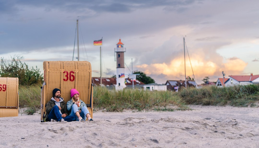 Paar sitzt im Strandkorb am Strand von Timmendorf auf Poel mit Blick auf Leuchtturm und Abendhimmel.