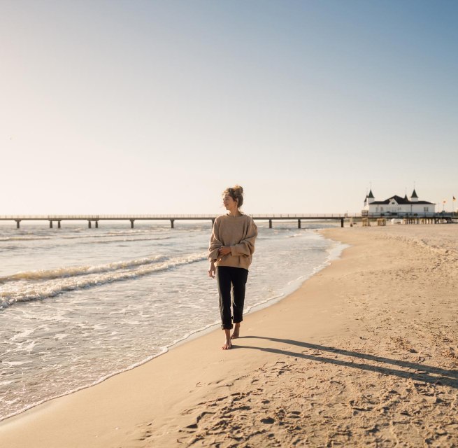 Frau spaziert am Strand von Ahlbeck zum Sonnenaufgang mit Seebr&uuml;cke im Hintergrund