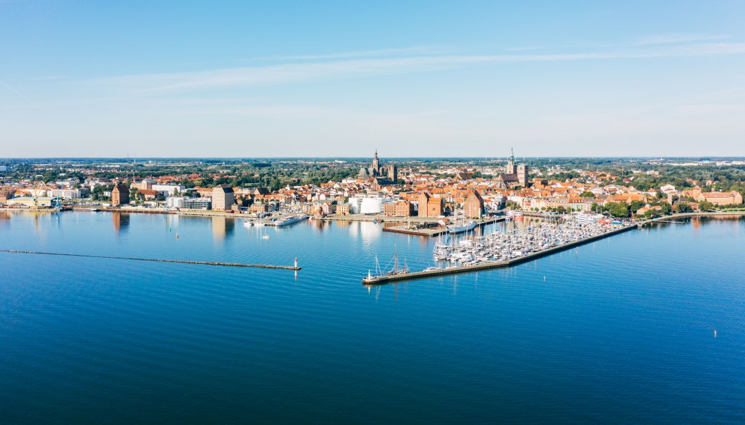 Luftaufnahme der Hansestadt Stralsund mit Hafen, historischer Altstadt und Ostsee bei blauem Himmel.