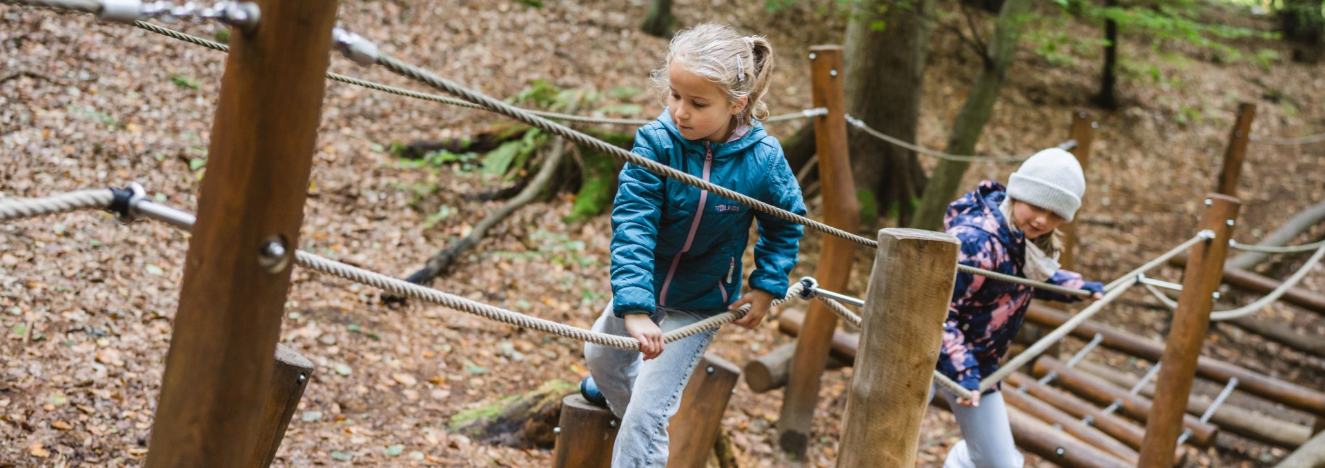 Zwei Kinder balancieren an einer Spielstation im Kinderheilwald Heringsdorf durch den herbstlichen Buchenwald auf Usedom.