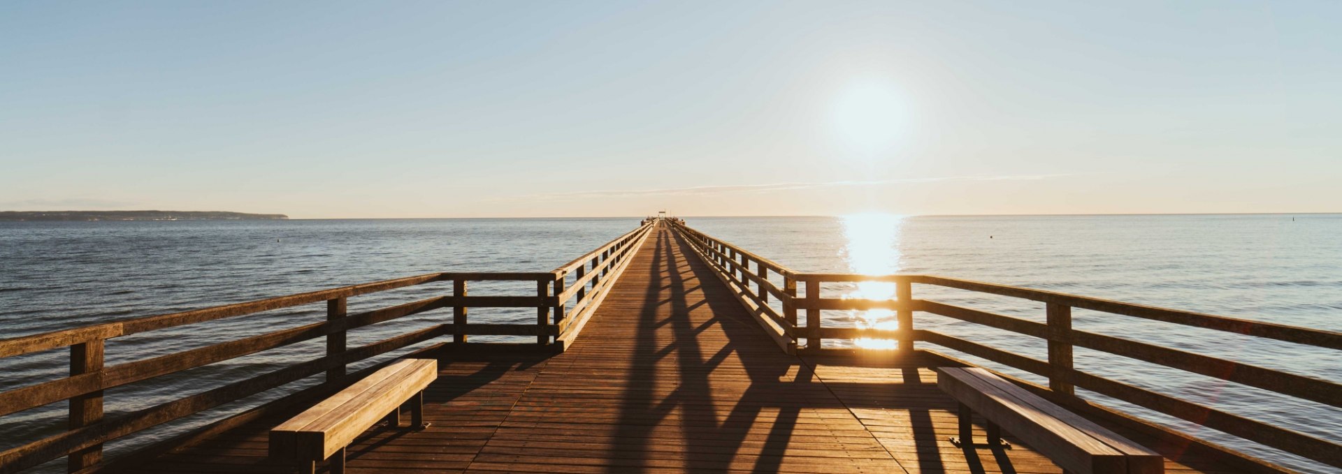 Sonnenaufgang &uuml;ber der Seebr&uuml;cke Binz, mit goldenen Reflexionen auf der Ostsee.