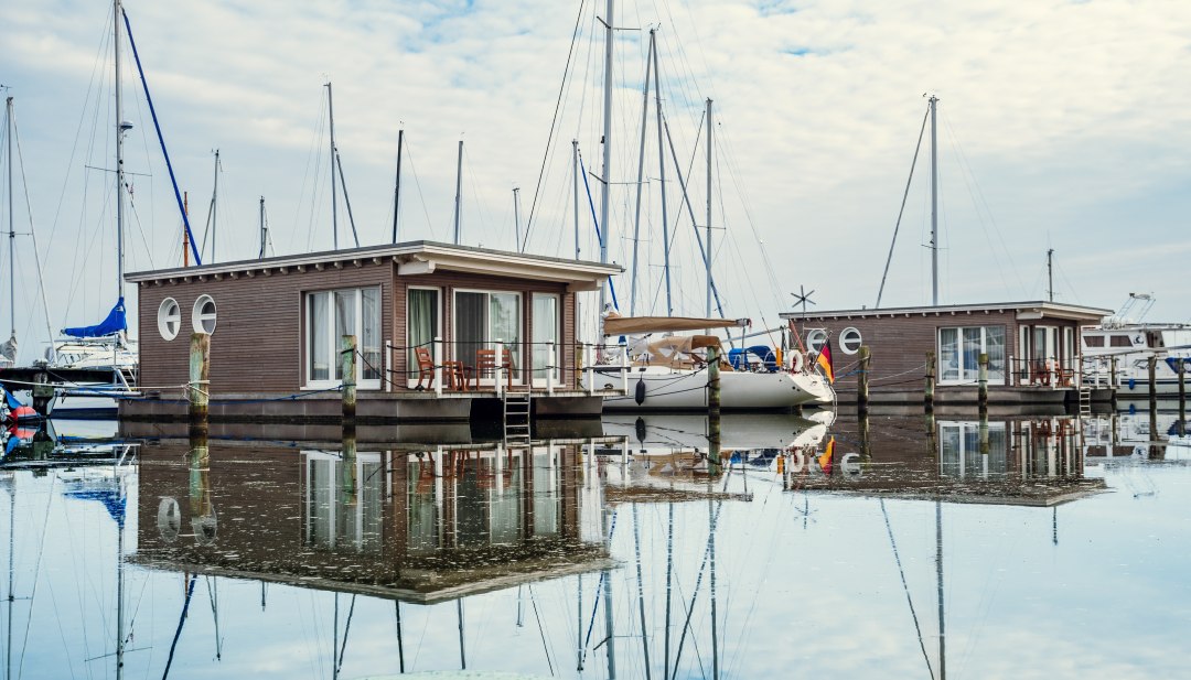 Hausboote und Segelboote liegen angeleint im Hafen von Krummin // Schwimmendes Urlaubsglück: Die im Stil von Hausbooten konstruierten Suiten sind fest verankert. // © MV-T/Tiemann Hausboote und Segelboote liegen angeleint im Hafen von Krummin