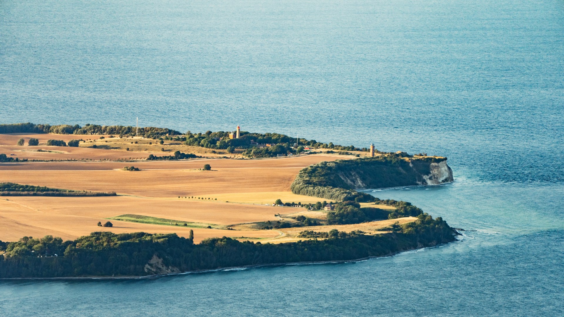 Luftaufnahme des Kap Arkona auf Rügen, die Leuchttürme und weite Felder zeigt, umgeben vom tiefblauen Meer der Ostsee.