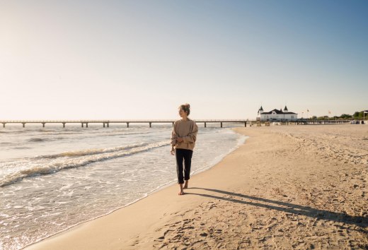 Frau spaziert am Strand von Ahlbeck zum Sonnenaufgang mit Seebrücke im Hintergrund // © MV-T/Petermann Frau spaziert am Strand von Ahlbeck zum Sonnenaufgang mit Seebrücke im Hintergrund