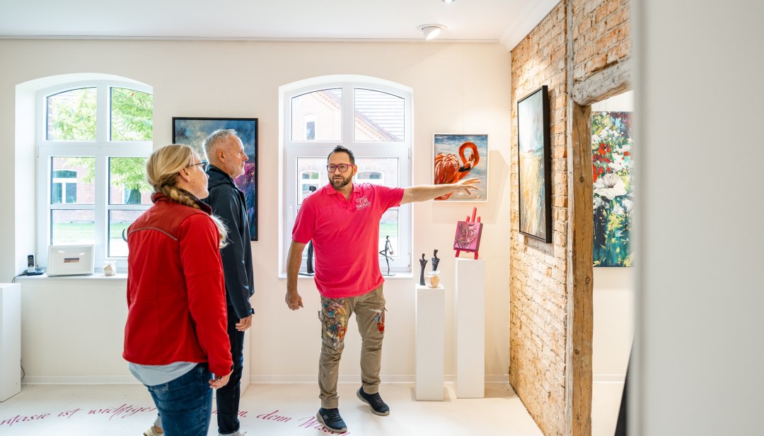 Kunstf&uuml;hrung in heller Galerie mit Besuchern vor Gem&auml;lden und freiliegenden Holzbalken in Basthorst.
