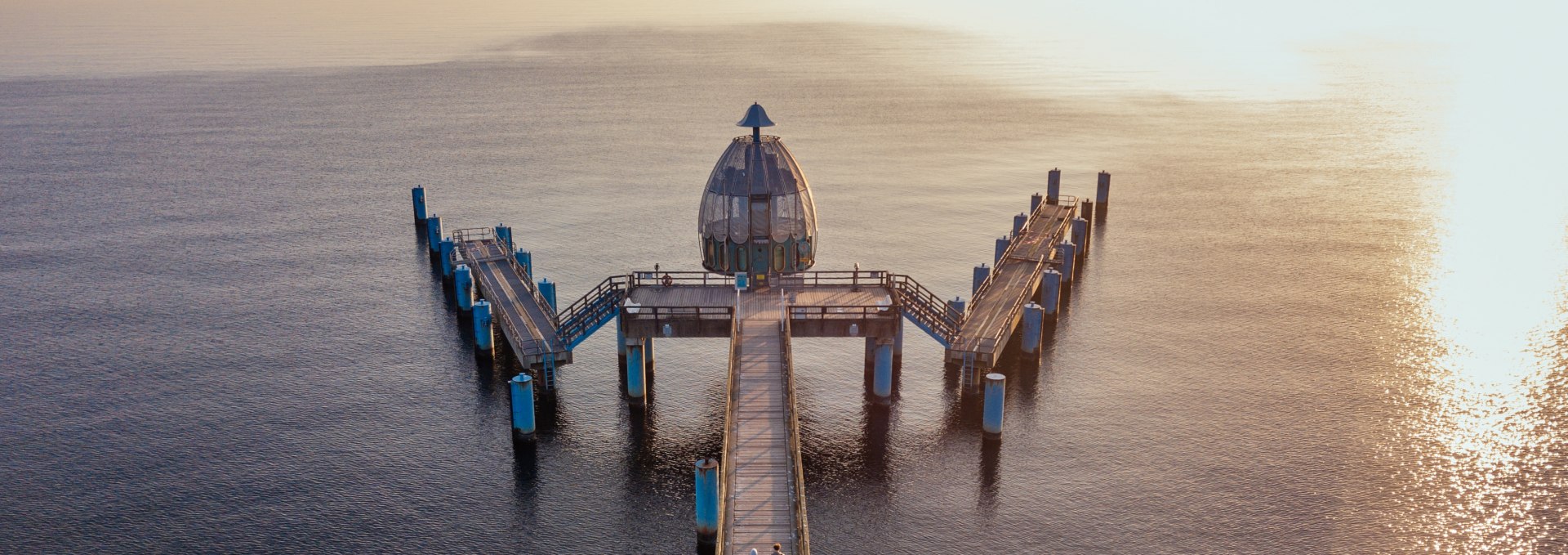 Drohnenaufnahme der Tauchgondel an der Seebrücke Sellin, mit Holzsteg und der Ostsee im goldenen Licht eines Sonnenuntergangs. // Die Tauchgondel an der Seebrücke Sellin: Ein faszinierender Ort für einen romantischen Spaziergang, umgeben von der Ruhe der Ostsee und einem spektakulären Sonnenuntergang. // © MV-T/Gänsicke Drohnenaufnahme der Tauchgondel an der Seebrücke Sellin, mit Holzsteg und der Ostsee im goldenen Licht eines Sonnenuntergangs.