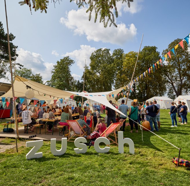 Menschen stehen unter einem mit bunten Wimpeln geschm&uuml;ckten  Sonnensegel // &copy; Oliver Borchert