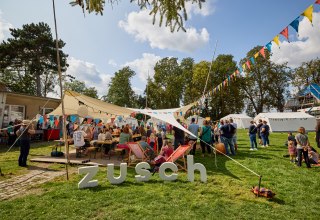 Menschen stehen unter einem mit bunten Wimpeln geschm&uuml;ckten  Sonnensegel // &copy; Oliver Borchert