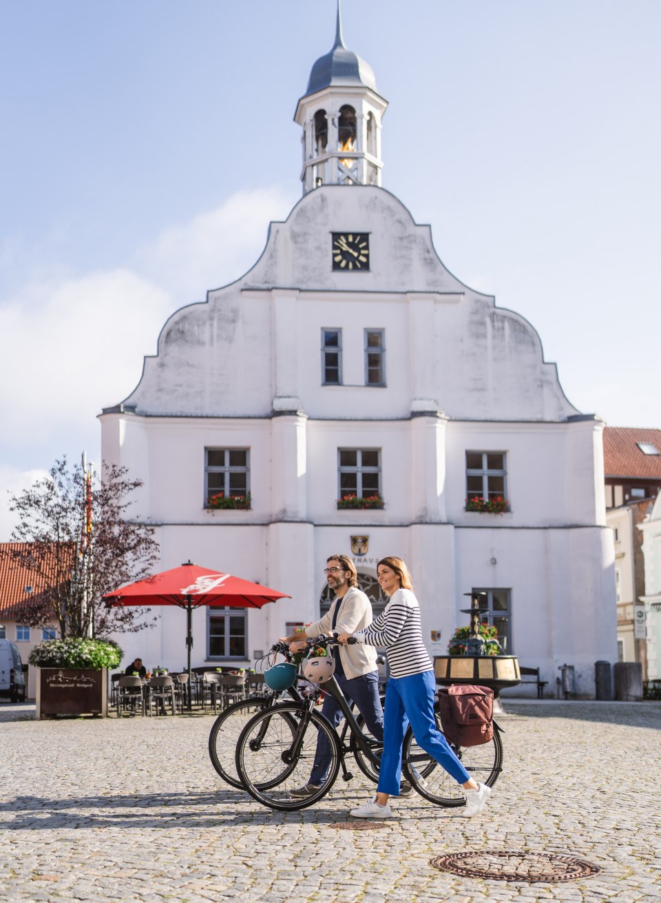 Zwei Fahrradfahrer schieben ihr Rad über den Marktplatz in Wolgast