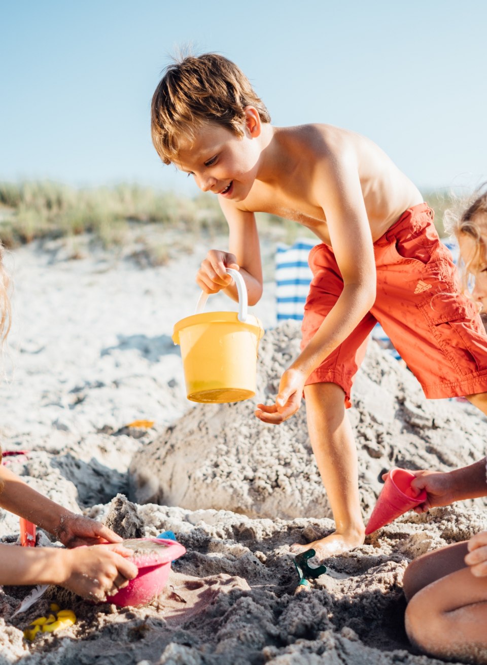 Drei Kinder spielen am Strand von Dierhagen im Sand, graben und bauen gemeinsam bei hellem Sonnenlicht.