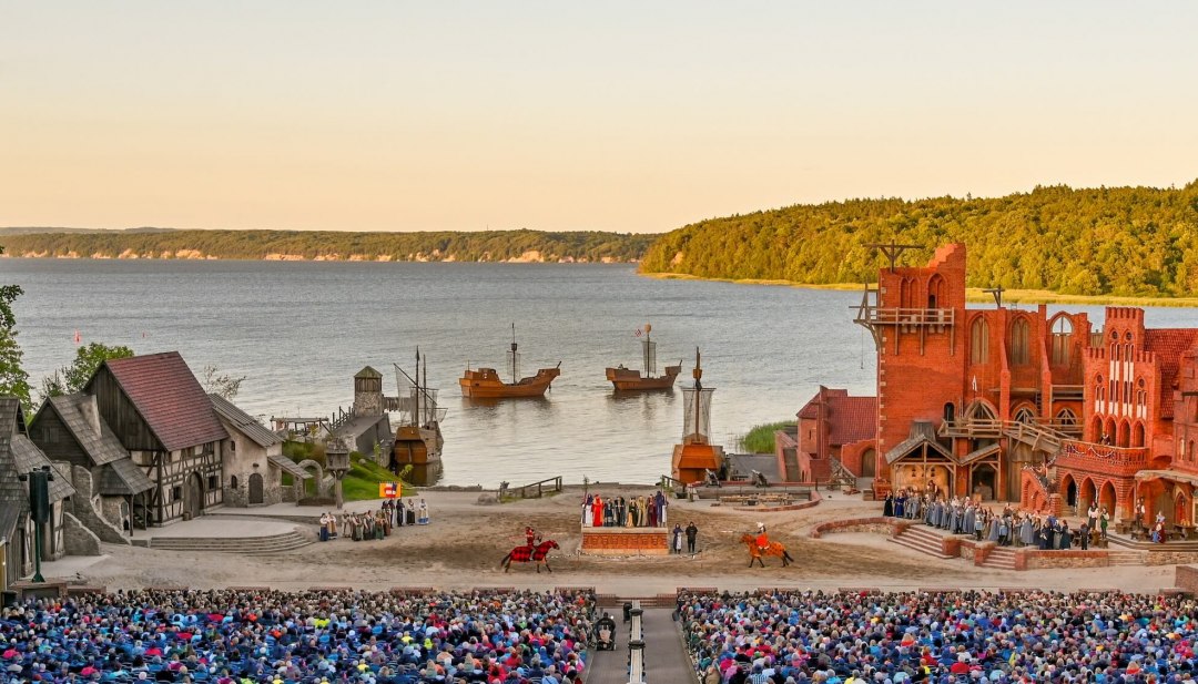 Bühne der Störtebeker Festspiele in Ralswiek auf Rügen mit Publikum, mittelalterlichen Kulissen und Blick auf die Ostsee.