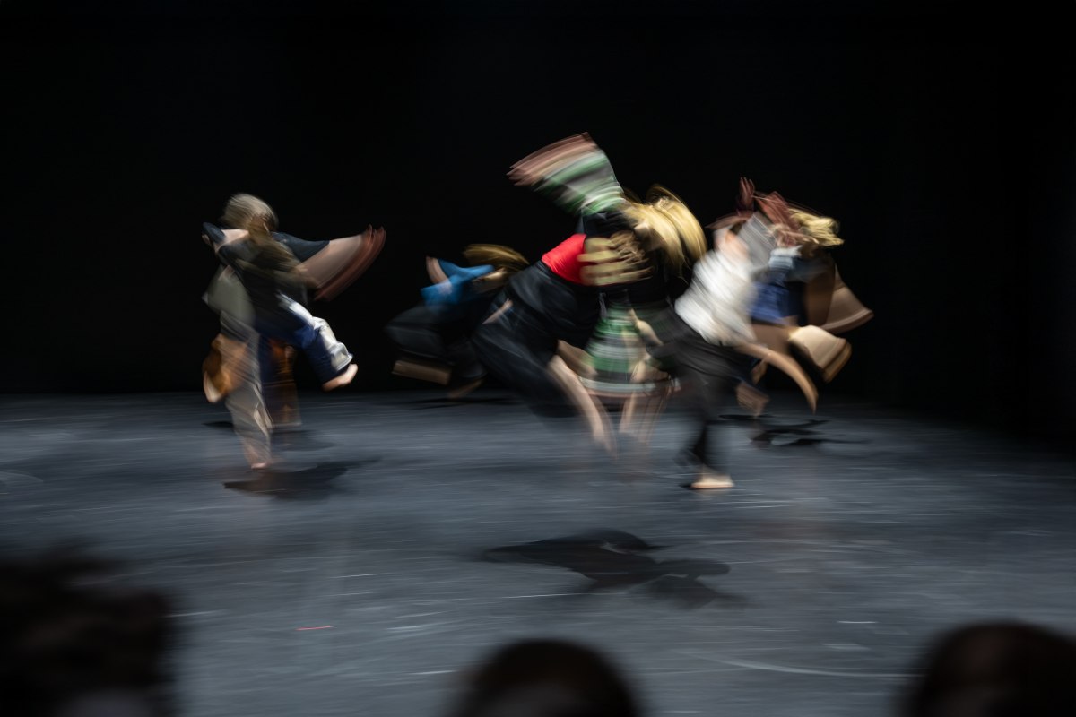 Eine Gruppe T&auml;nzerinnen im Sprung mit schwingenden Armen auf einer B&uuml;hne. Auf dem schwarzen Boden ist ein Schatten einer T&auml;nzerin gut sichtbar. // &copy; Jonas Zeidler