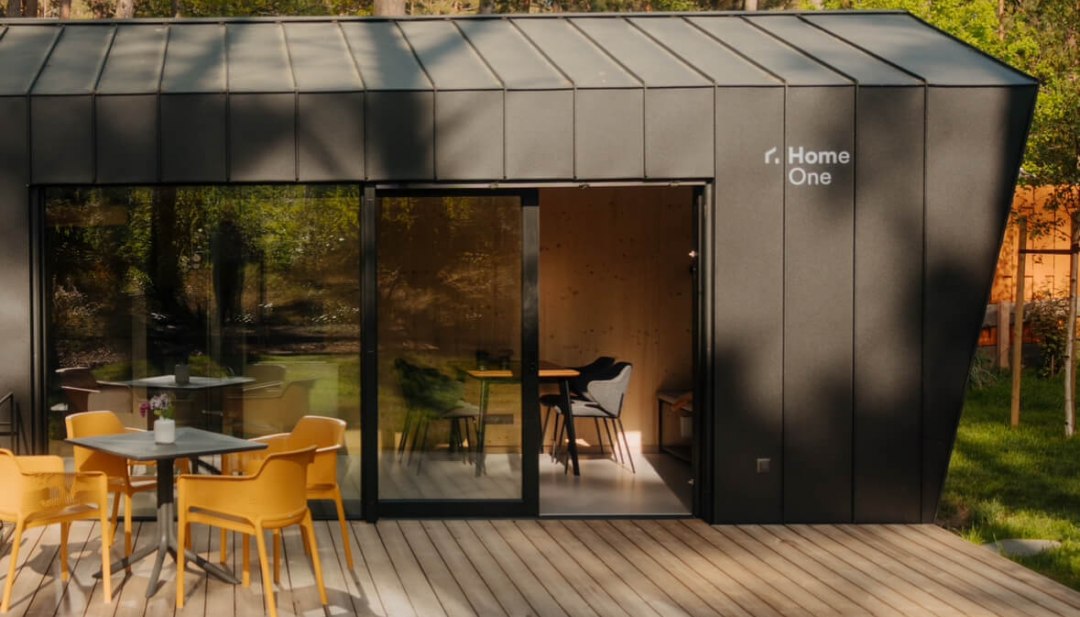 Natur trifft Design – stilvolles Tiny House mitten im Wald für eine entspannte Auszeit mit Komfort und Ruhe., © Cabin28 Modernes Tiny House mit dunkler Fassade, großer Holzterrasse und Outdoor-Sitzbereich, idyllisch im Wald gelegen.