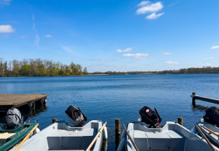 Blick vom Bootssteg &uuml;ber den Krakower See bei strahlendem Sonnenschein. Im Vordergrund liegen mehrere Ruder- und Motorboote der Bootsvermietung der Feriensiedlung Kiefernhain am Steg, Im Hintergrund erstreckt sich die weite, ruhige Wasserfl&auml;che mit bewaldeten Ufern. // &copy; Feriensiedlung Kiefernhain