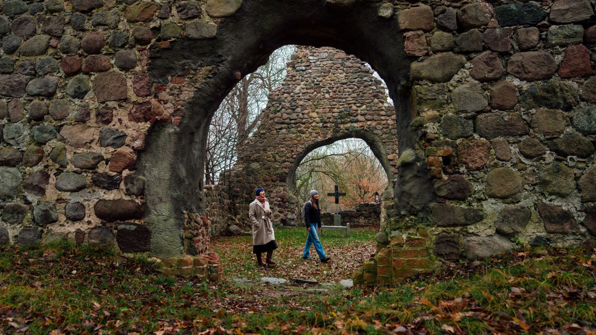 Entdeckertour zur Ruine Wüste Kirche in Ulrichshusen – historische Mauern, malerische Bögen und herbstliche Stimmung machen diesen Ort zu einem besonderen Ausflugsziel., © TMV/Petermann Zwei Personen erkunden die Ruine Wüste Kirche in Ulrichshusen, umgeben von Steinbögen, herbstlichem Laub und kahlen Bäumen.
