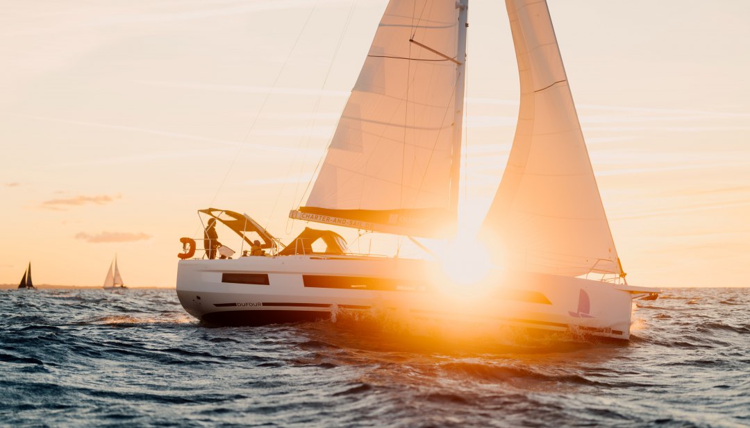 Segelboot mit orangefarbenen Segeln auf der Ostsee vor Warnem&uuml;nde bei Sonnenuntergang.