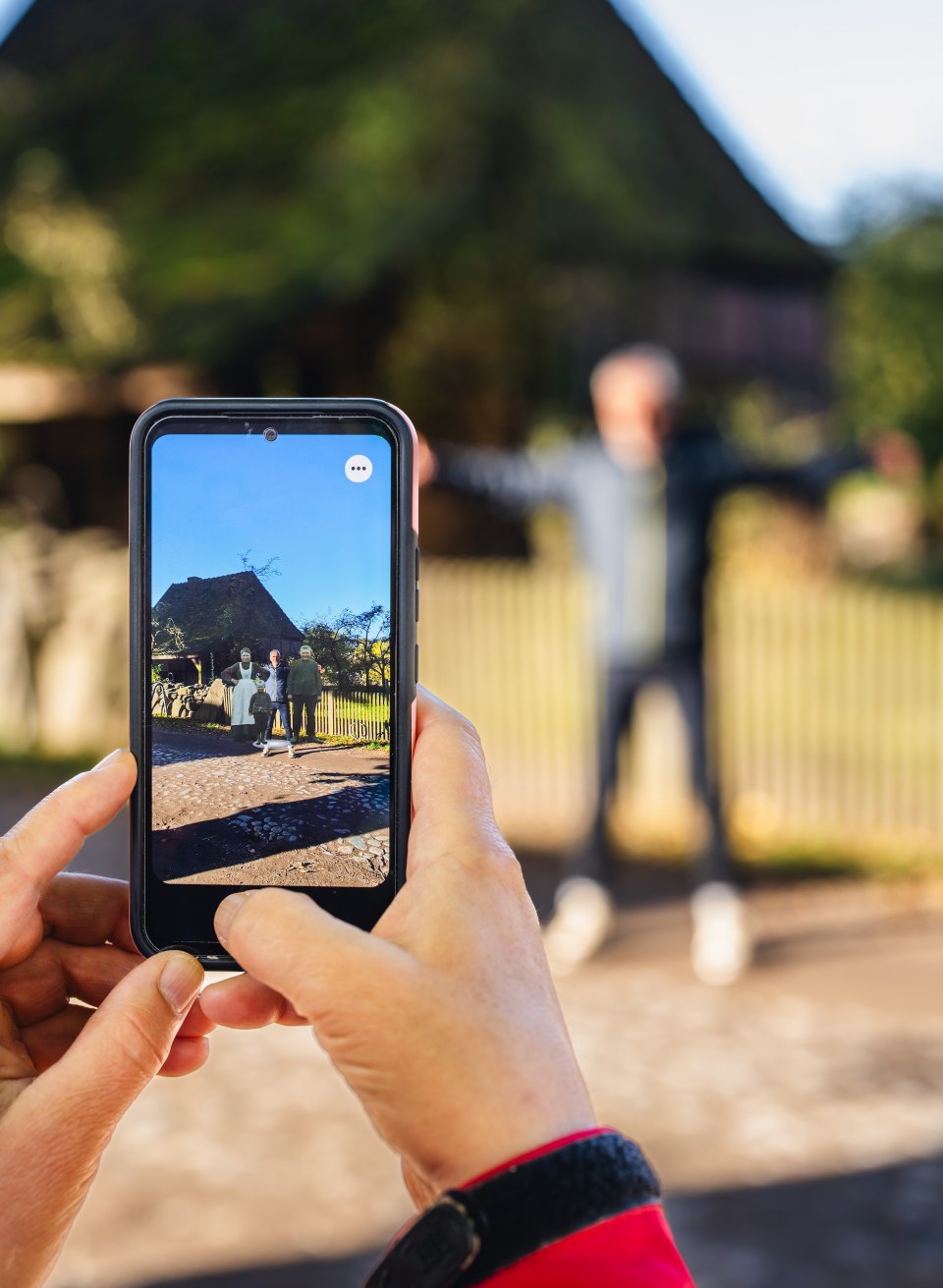 Museum interaktiv erleben – Augmented Reality bringt Geschichte zum Leben im Freilichtmuseum für Volkskunde Schwerin-Mueß., © TMV/Gross Eine Person fotografiert mit einem Smartphone ein historisches Gebäude im Freilichtmuseum Schwerin-Mueß, während eine andere im Hintergrund posiert.