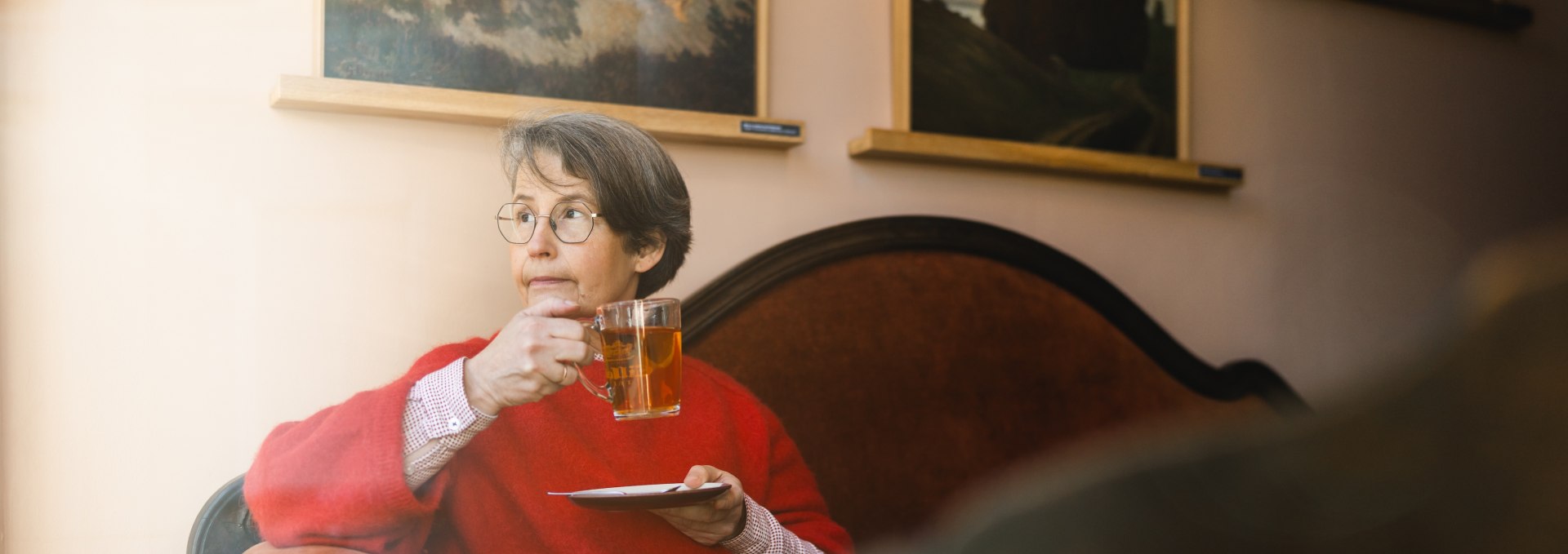 Frau mit Tee im gem&uuml;tlichen Caf&eacute; Gertrud in Greifswald, umgeben von Kunstwerken an den W&auml;nden.
