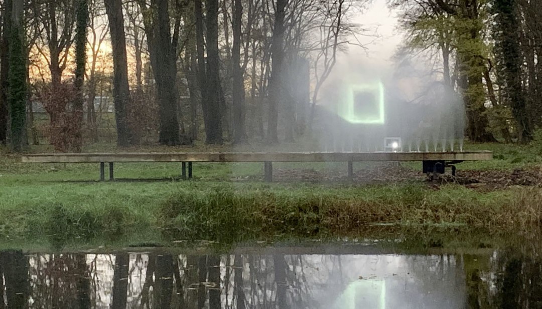 Leuchtende Lichtinstallation auf Wassernebel im Park mit Spiegelung im Teich w&auml;hrend der Veranstaltungsreihe KUNST HEUTE.
