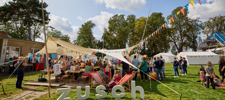 Menschen stehen unter einem mit bunten Wimpeln geschm&uuml;ckten  Sonnensegel // &copy; Oliver Borchert