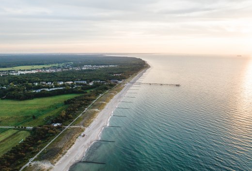 Luchtfoto van de pier en het strand van Graal-M&uuml;ritz, omgeven door bossen en weilanden, met de Baltische Zee in het licht van een sfeervolle zonsondergang.