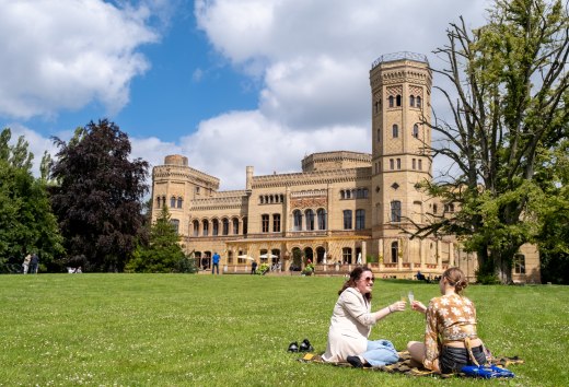 Zwei Frauen genießen ein Picknick auf einer Wiese vor dem Schloss Schloss Neetzow während der MittsommerRemise an einem sonnigen Tag.