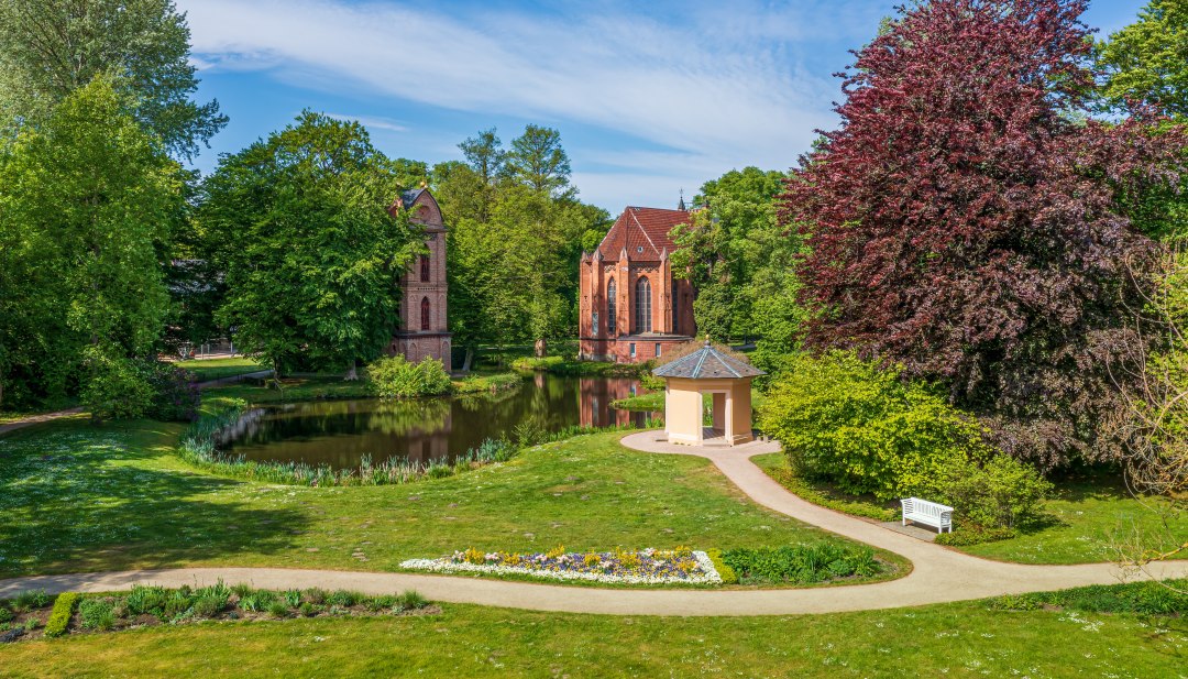 Glockenturm und Parkgebäude im Schlossgarten Ludwigslust mit Blumen und Bäumen. // Der erste neogotische Kirchenbau Mecklenburgs, ein einzelnstehender Glockenturm und das älteste Parkgebäude: Im Prinzengarten, direkt neben dem Schloss, liegen mehrere Highlights des Ludwigsluster Schlossgartens. // © MV-T/Tiemann Glockenturm und Parkgebäude im Schlossgarten Ludwigslust mit Blumen und Bäumen.