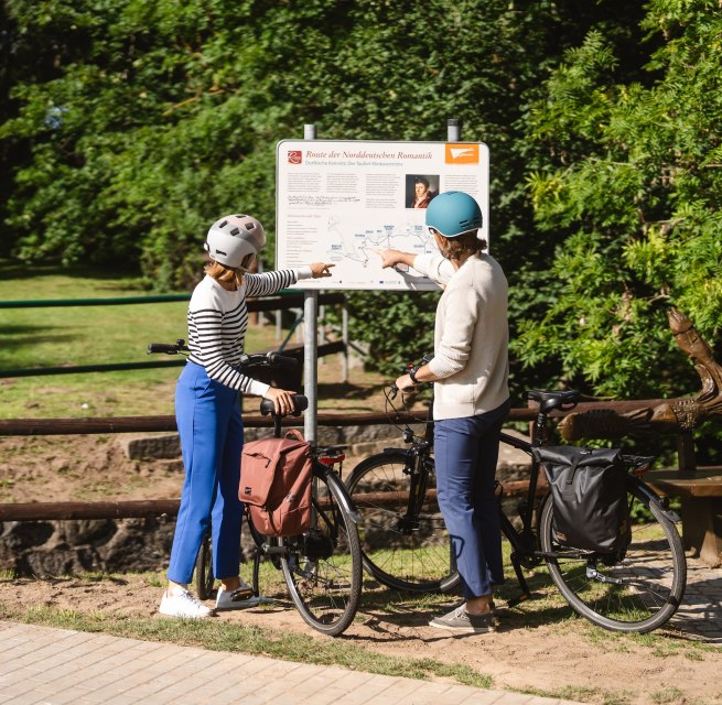 Twee fietsers staan bij het bord voor de Route van de Noord-Duitse Romantiek