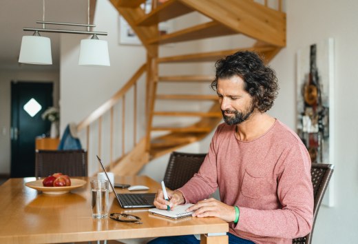 Ein Mann sitzt an einem Holztisch in einem Ferienhaus, arbeitet am Laptop und macht Notizen – ideale Bedingungen für eine Workation auf der Insel Poel. // Workation auf der Insel Poel: Im gemütlichen Ferienhaus produktiv arbeiten und die Auszeit genießen. // © MV-T/Gross Ein Mann sitzt an einem Holztisch in einem Ferienhaus, arbeitet am Laptop und macht Notizen – ideale Bedingungen für eine Workation auf der Insel Poel.