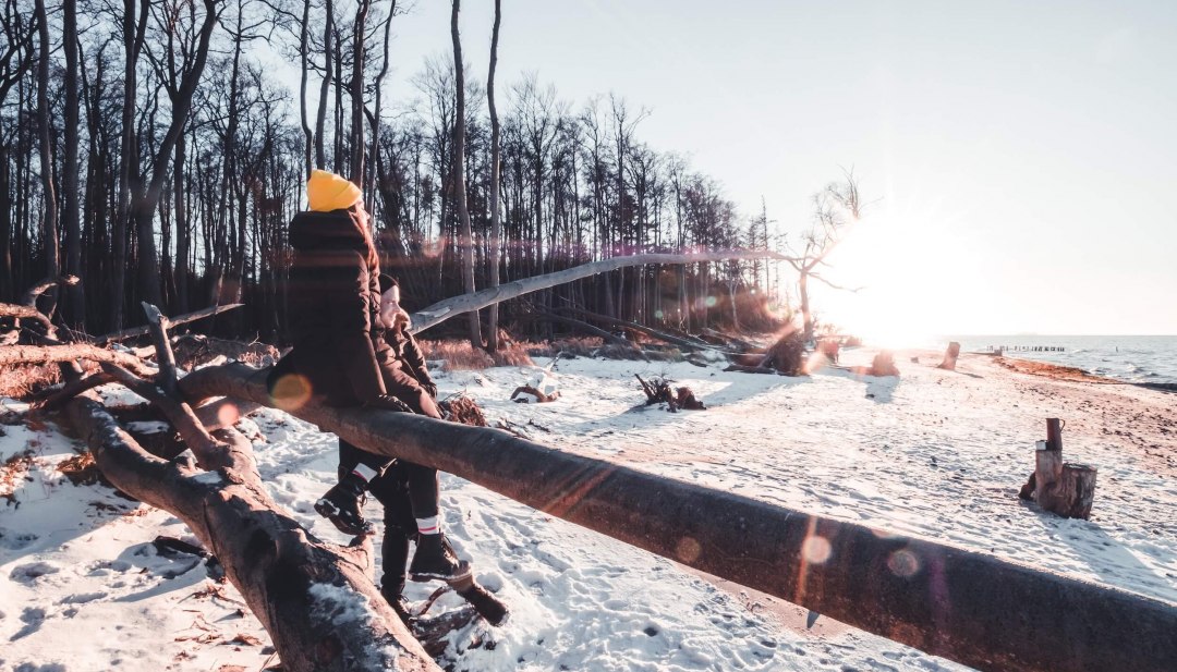 Entlang der verschneiten Ostseeküste bei Torfbrücke eintauchen in die stille Winterlandschaft und die kraftvolle Natur spüren., © TMV/Scholz-Winter Zwei Personen in Winterkleidung wandern auf einem schneebedeckten Ostseestrand von Torfbrücke bei Sonnenuntergang.