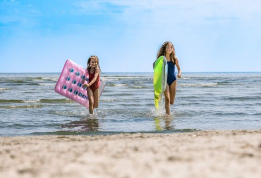 Zwei Kinder laufen aus dem Wasser an den Strand mit Luftmatratzen unter dem Arm