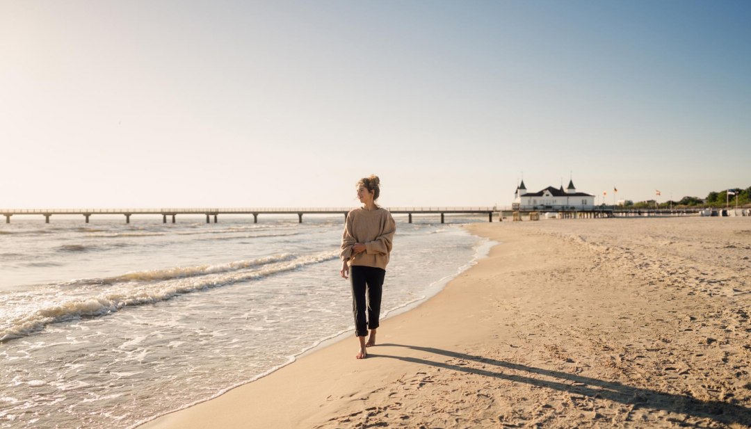 Frau spaziert am Strand von Ahlbeck zum Sonnenaufgang mit Seebr&uuml;cke im Hintergrund