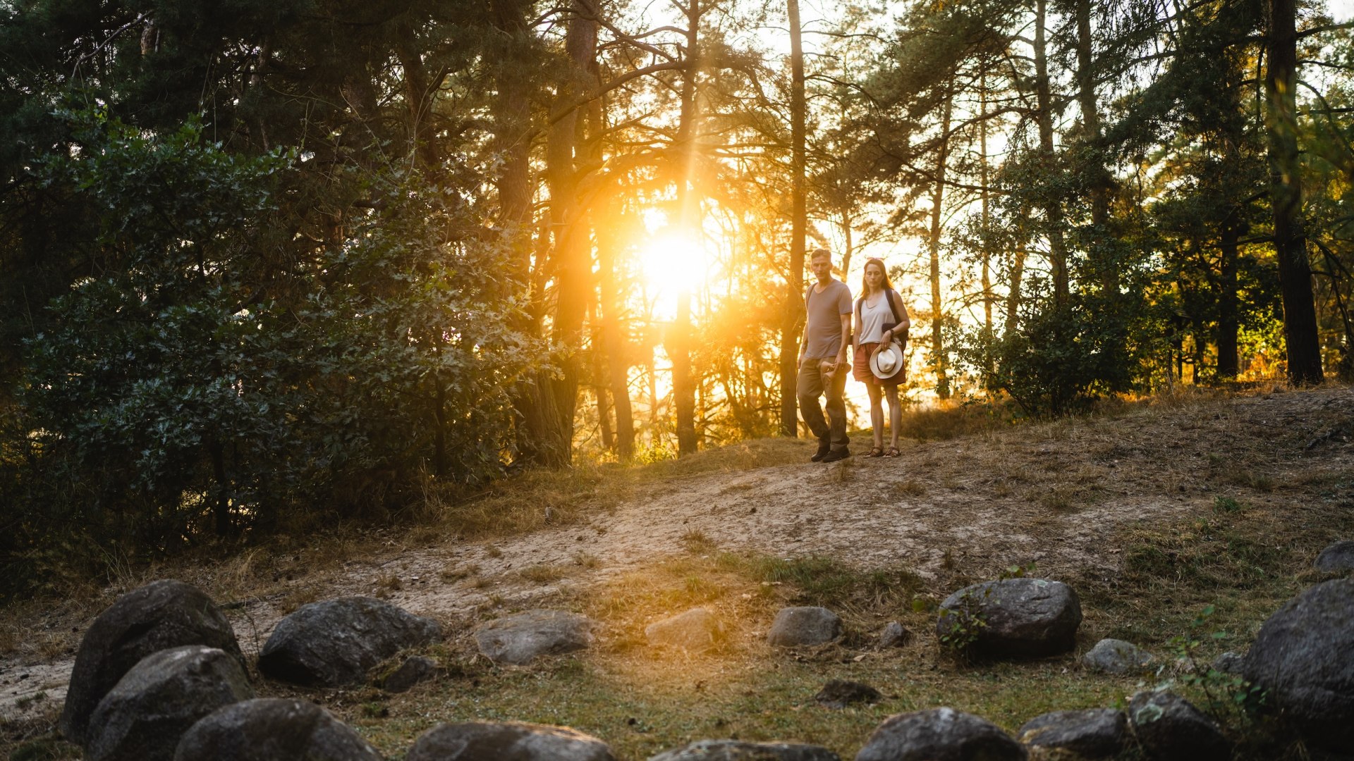 Een stel wandelt in de schemering naar de historische Vikinggraven bij Menzlin, omringd door bomen en warm licht.