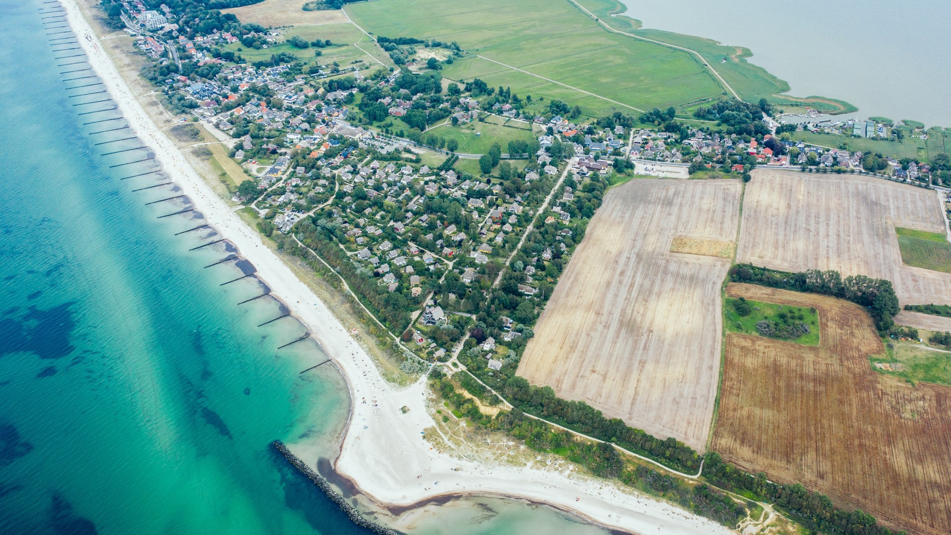 Luftaufnahme einer K&uuml;stenlandschaft auf R&uuml;gen mit Strand, Feldern, gr&uuml;nen Wiesen und klar t&uuml;rkisfarbenem Ostseewasser.