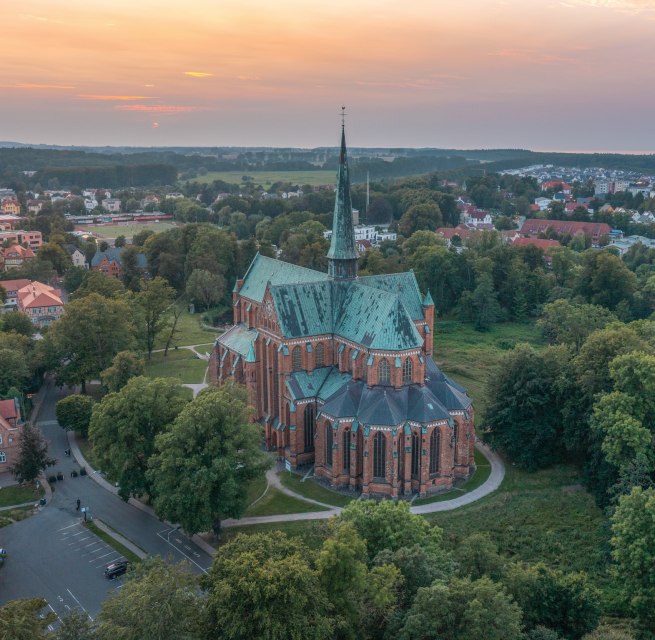 Luftaufnahme des M&uuml;nsters in Bad Doberan bei Sonnenuntergang, umgeben von B&auml;umen, Wiesen und der umliegenden Stadt.