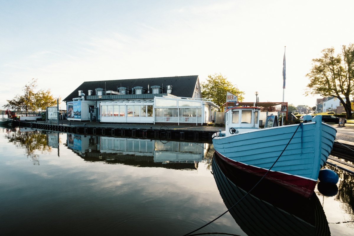 Restaurant Ribnitzer Fischhafen aan het water: een boot aan de steiger, een spiegelglad wateroppervlak &ndash; havenflair die uitnodigt tot een pauze. // &copy; Ribnitzer Fischhafen/Hugo Scholz-Witzel