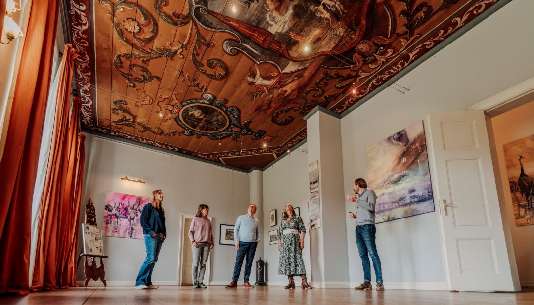 Gasten staan in de barokke hal en kijken naar het rijk beschilderde plafond met ornamenten in het landhuis van Ludorf.