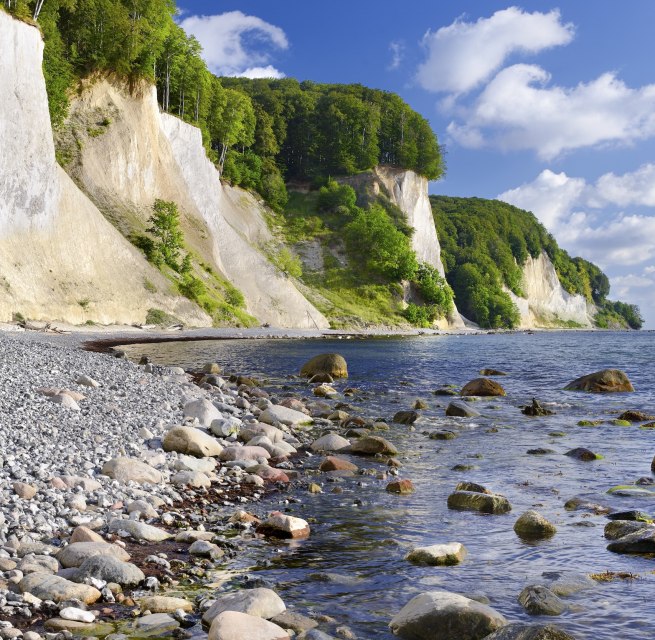Runde Steine s&auml;umen den Strand, sanfte Wellen umsp&uuml;len moosbedeckte Findlinge. Die wei&szlig;en Kreidefelsen des Nationalparks Jasmund ragen majest&auml;tisch &uuml;ber der Ostsee auf, gekr&ouml;nt von sattem Buchengr&uuml;n. Ein Ort, an dem Stille h&ouml;rbar wird und die Kraft der Natur sp&uuml;rbar bleibt. // &copy; Francesco Carovillano