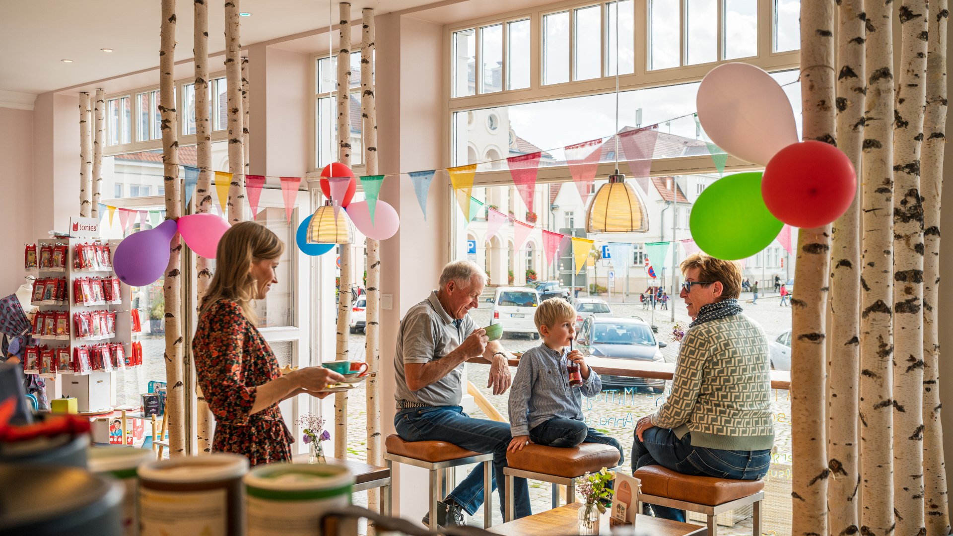 Grootouders en kleinkinderen drinken koffie aan de hoge tafel met uitzicht naar buiten. // Grootouders en kleinkinderen kunnen genieten van versnaperingen in het Anna & Otto familiecafé - waar de kleine Friedrich ook een spelletje kan spelen. // © MV-T/Tiemann Grootouders en kleinkinderen drinken koffie aan de hoge tafel met uitzicht naar buiten.