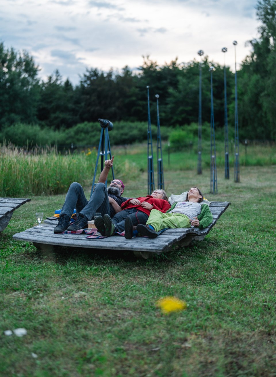 Drei Personen liegen auf einer Holzplattform im Gr&uuml;nen und blicken in den Abendhimmel, Sternenpark Mecklenburg-Vorpommern.