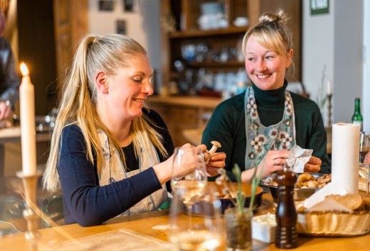 Zwei Frauen bereiten in der K&uuml;che im Gutshaus Ehmkendorf gemeinsam ein Essen zu, Kerzenlicht und Holzregale im Hintergrund.