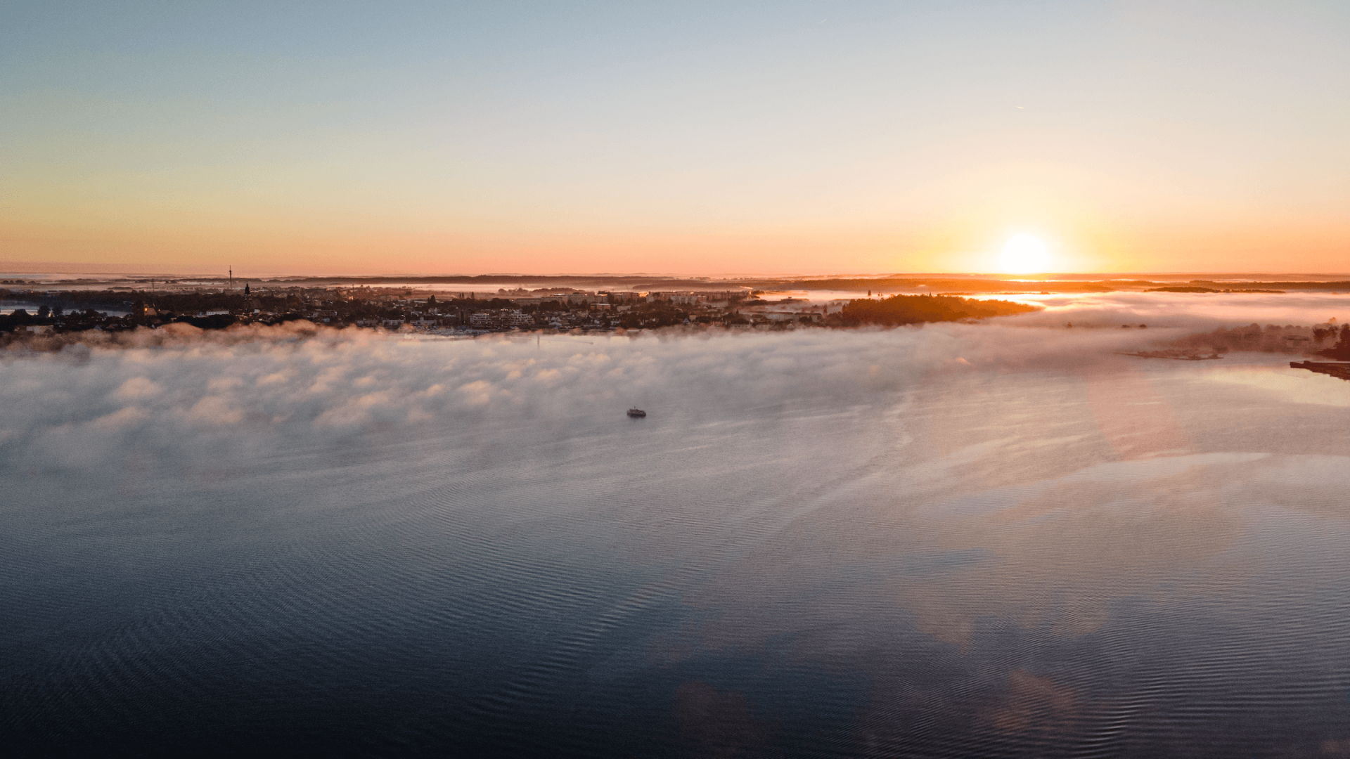 Neem een woonboot en bekijk de zonsopgang boven de M&uuml;ritz met mist over het water en uitzicht op de stad Waren in Mecklenburg-Vorpommern.