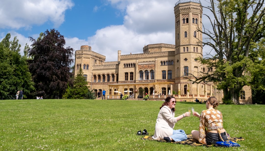 Zwei Frauen genießen ein Picknick auf einer Wiese vor dem Schloss Schloss Neetzow während der MittsommerRemise an einem sonnigen Tag.