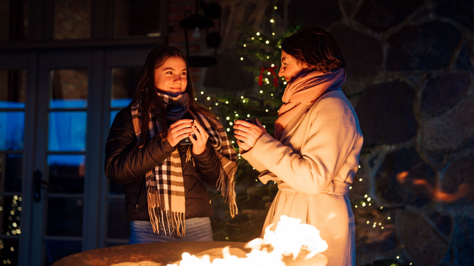 Zwei Frauen w&auml;rmen sich an einer Feuerschale auf dem Adventsmarkt im Schloss Ulrichshusen, umgeben von Lichterglanz und winterlicher Stimmung.
