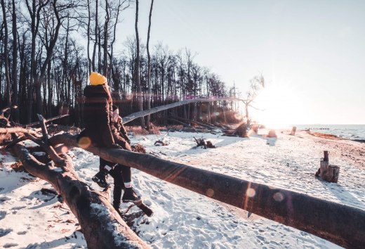 Zwei Personen in Winterkleidung wandern auf einem schneebedeckten Ostseestrand von Torfbr&uuml;cke bei Sonnenuntergang.
