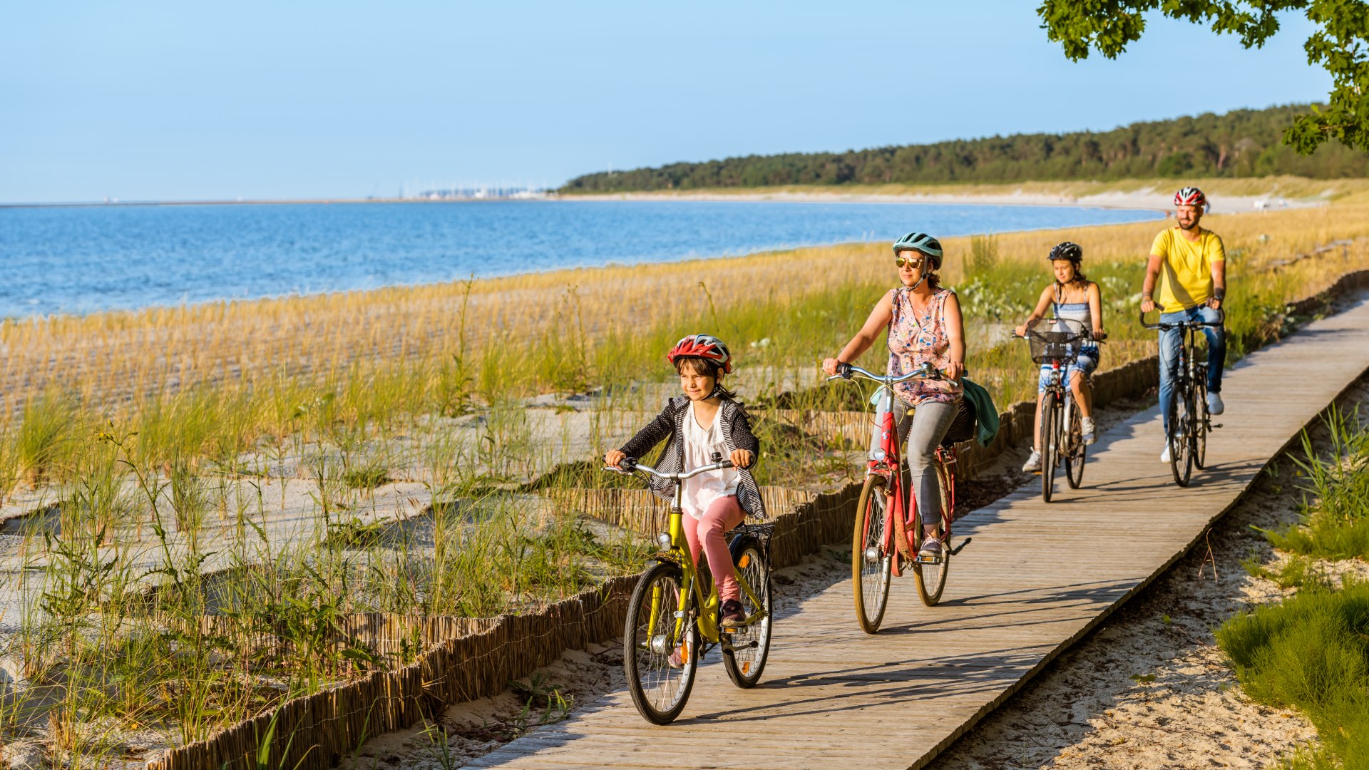 Eine vierk&ouml;pfige Familie f&auml;hrt mit dem Fahrrad auf dem Radweg am Strand entlang.